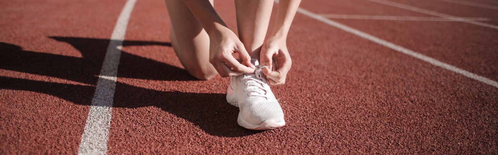 close up photo of woman tying her white sneakers on running track
