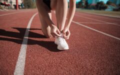 close up photo of woman tying her white sneakers on running track