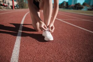 close up photo of woman tying her white sneakers on running track