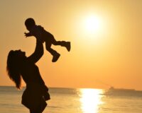 silhouette photo of a mother carrying her baby at beach during golden hour